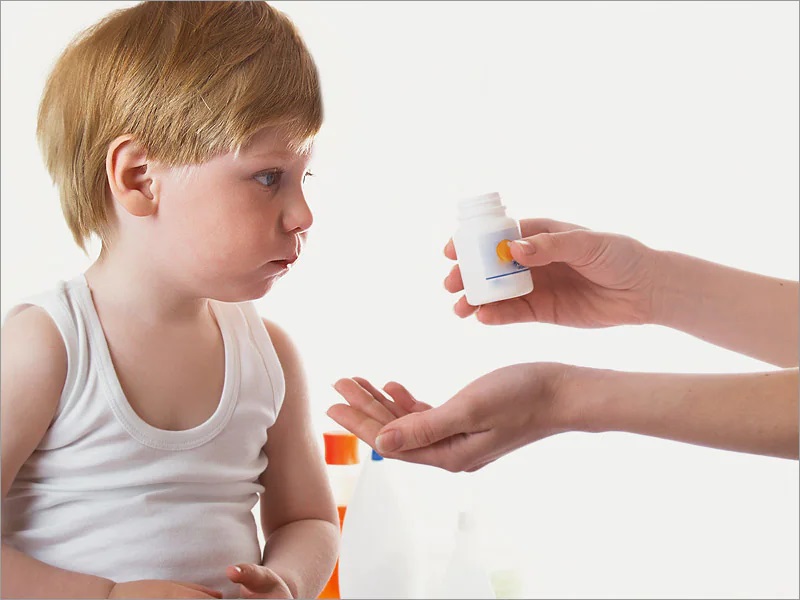 A mother holds a boy’s autism medication out in front of him to take.